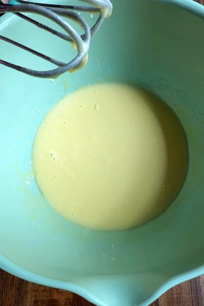 Smooth pale wet mixture in a light green bowl after the eggs, oil, sugar, and vanilla have been whisked until blended.