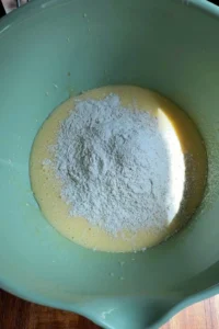 Dry ingredients added into the wet mixture, with a mound of flour mixture sitting on top before folding into the carrot cupcake batter.