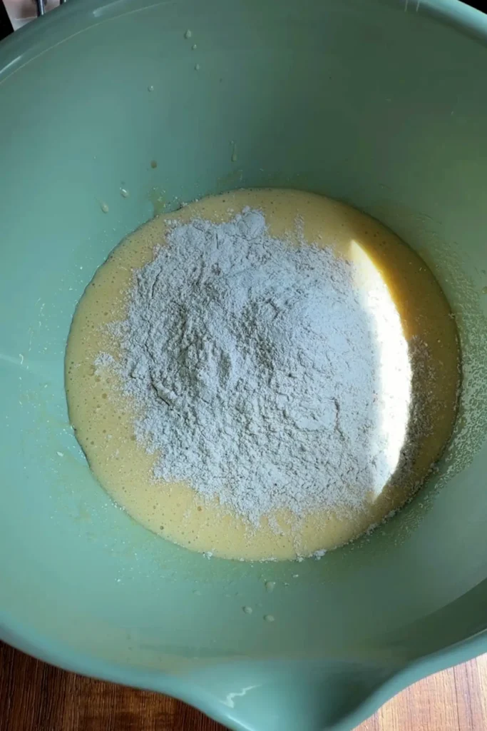 Dry ingredients added into the wet mixture, with a mound of flour mixture sitting on top before folding into the carrot cupcake batter.