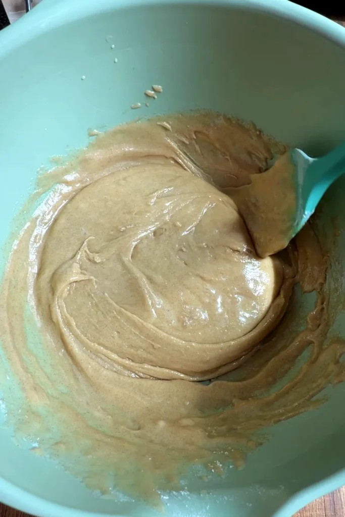 Thick tan cupcake batter being mixed with a spatula after the wet and dry ingredients are combined, showing a smooth and slightly glossy texture.