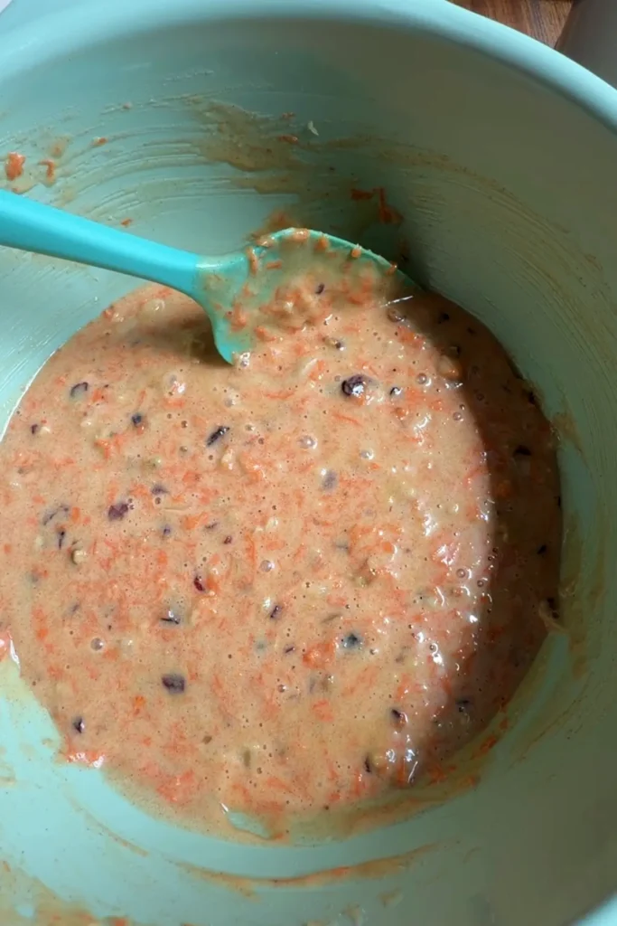 Finished carrot cupcake batter mixed in a large bowl, speckled with shredded carrots, nuts, pineapple, and dried cranberries.