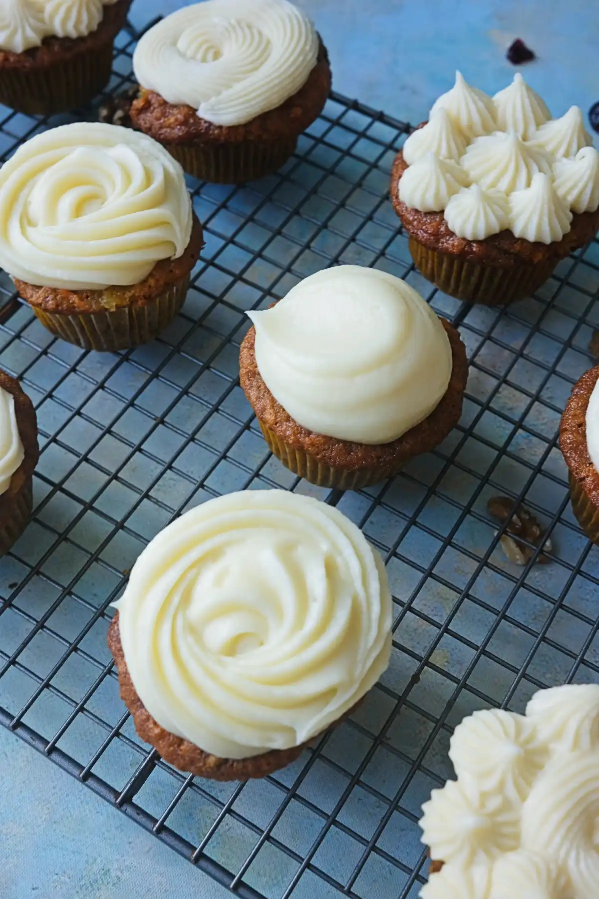 Several carrot cake cupcakes with cream cheese frosting arranged on a wire cooling rack.