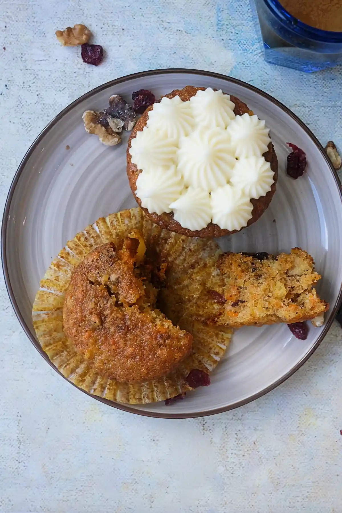 Overhead view of a plated carrot cake cupcake with one frosted cupcake topped with cream cheese and one cupcake split open to show the soft, textured interior.
