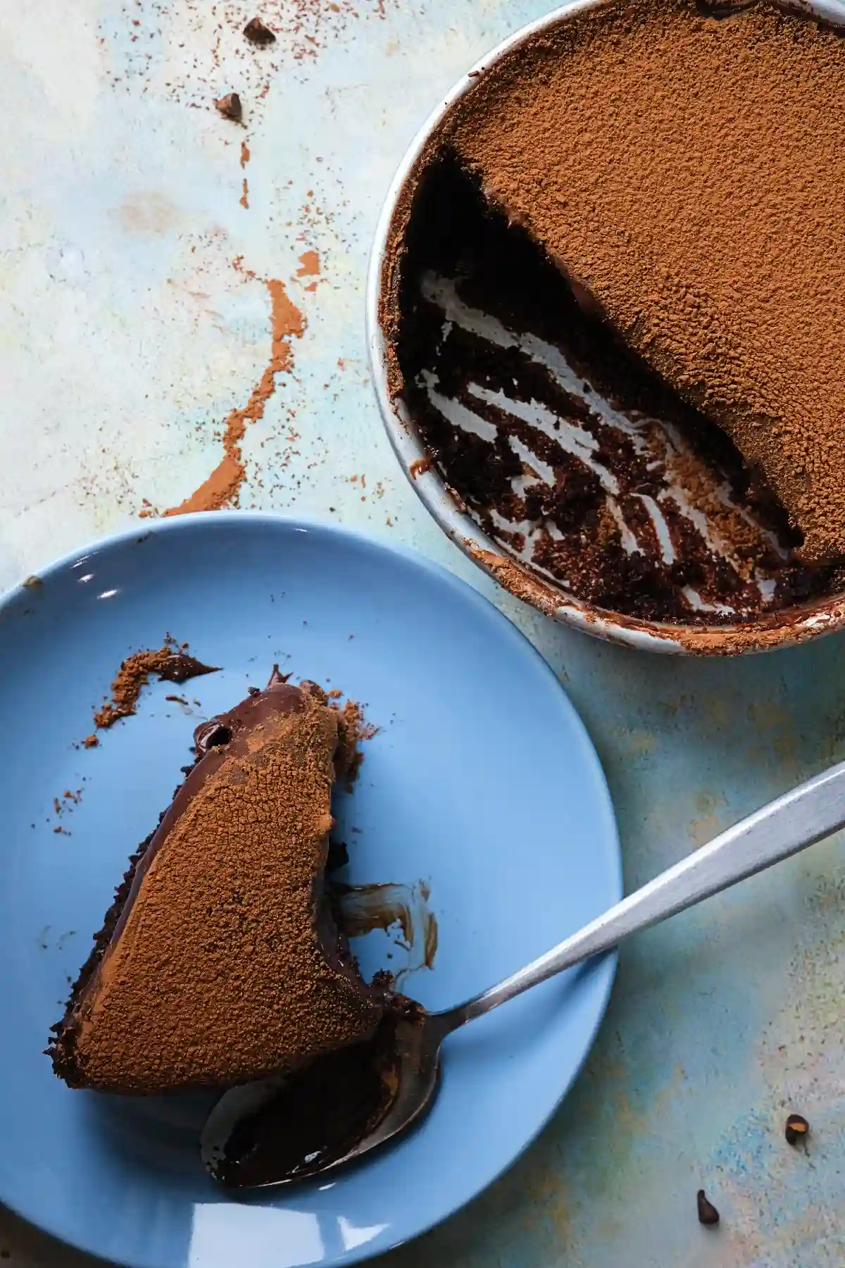 Overhead view of a chocolate dream cake with a slice removed, showing layers of moist cake and ganache, with cocoa powder scattered around the pan and on the surface.