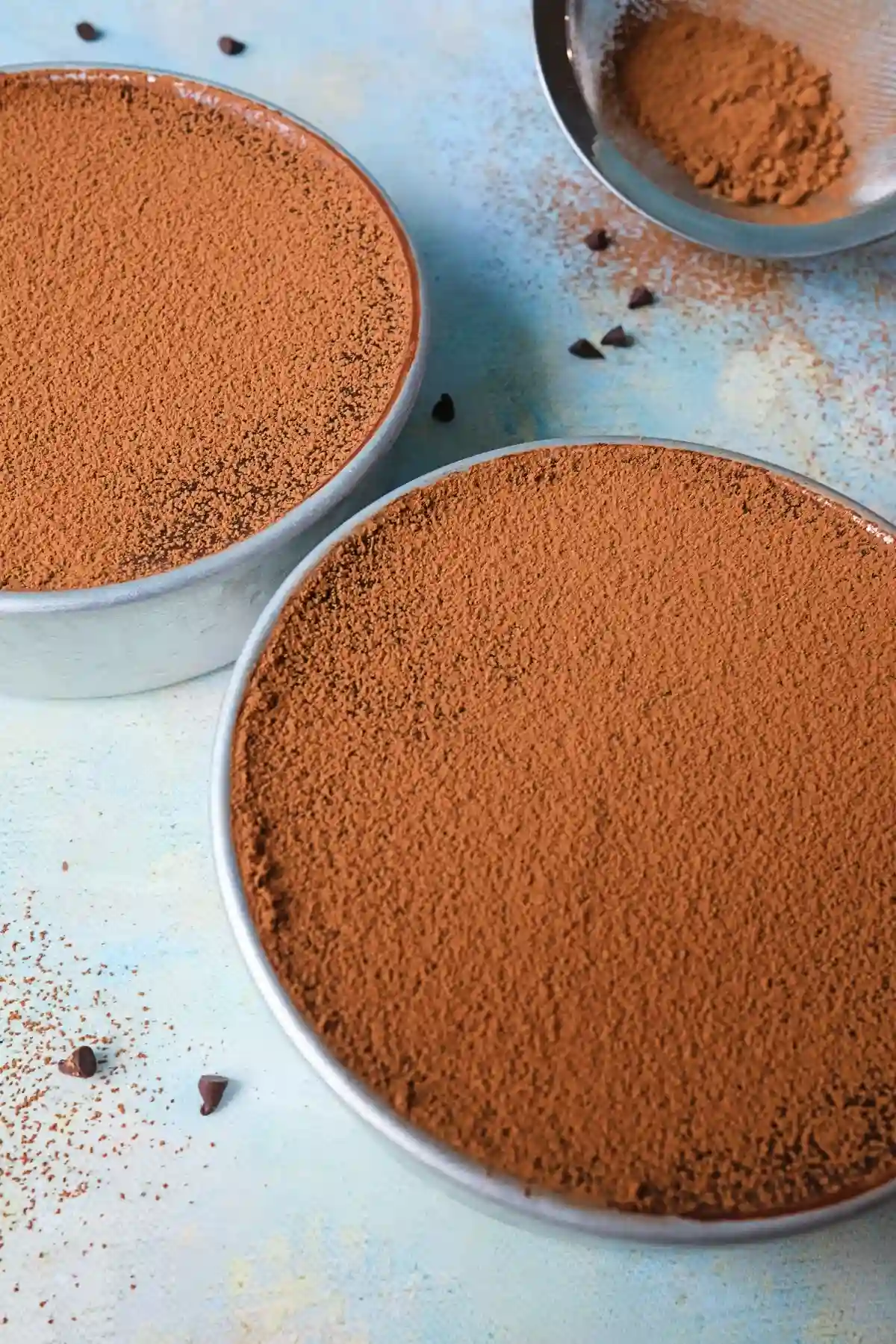 Slice of chocolate dream cake on a blue plate beside the remaining cake, with cocoa powder dusted on top and chocolate crumbs scattered on the plate.