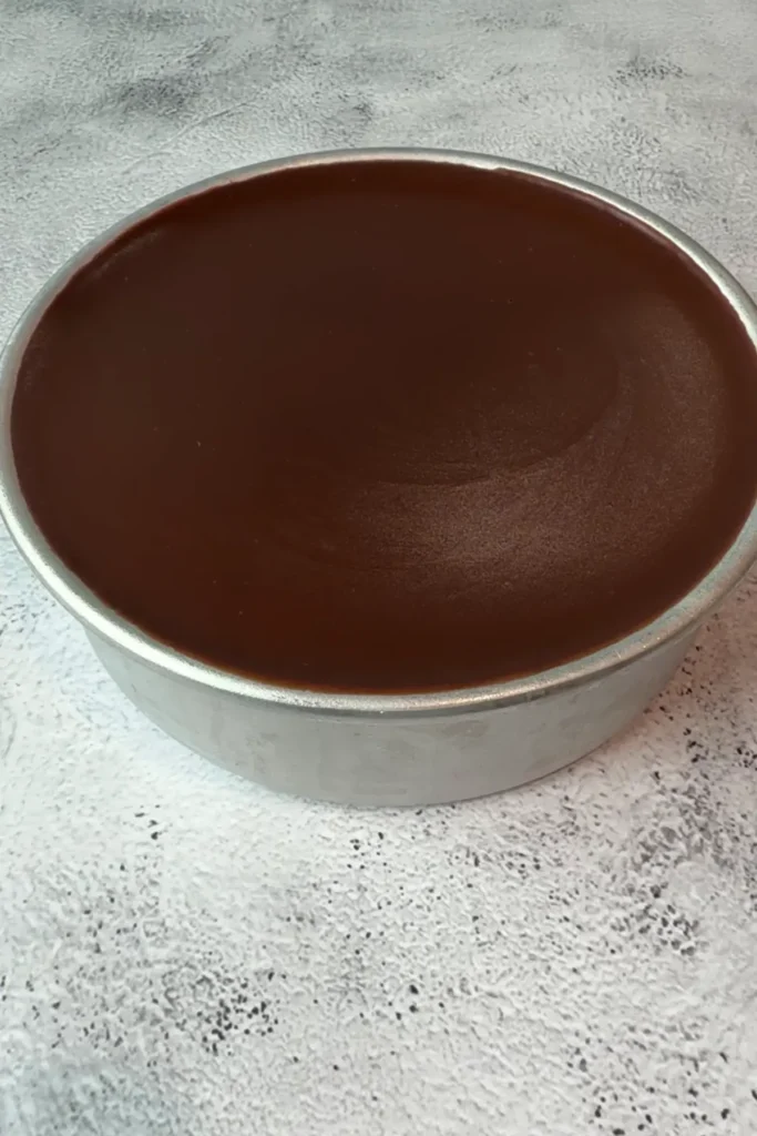 Finished chocolate dream cake in a pan with a smooth ganache topping, set and evenly spread across the surface.