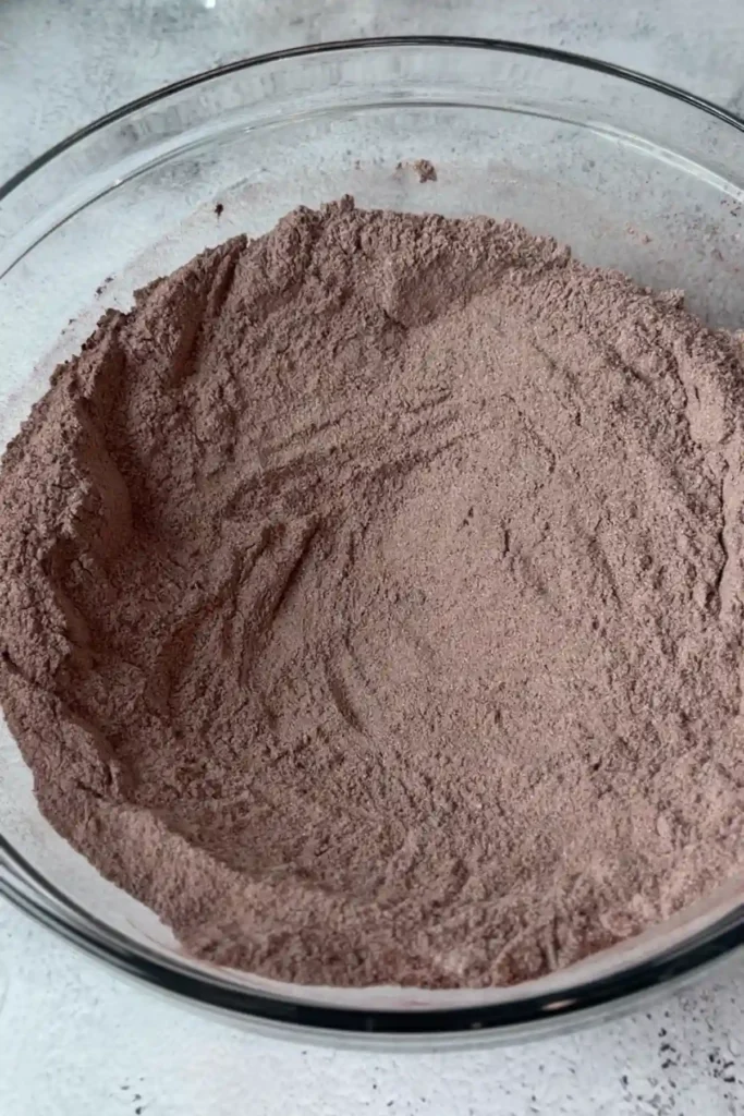 Bowl of sifted dry ingredients fully combined into a light, even cocoa mixture with no visible lumps.