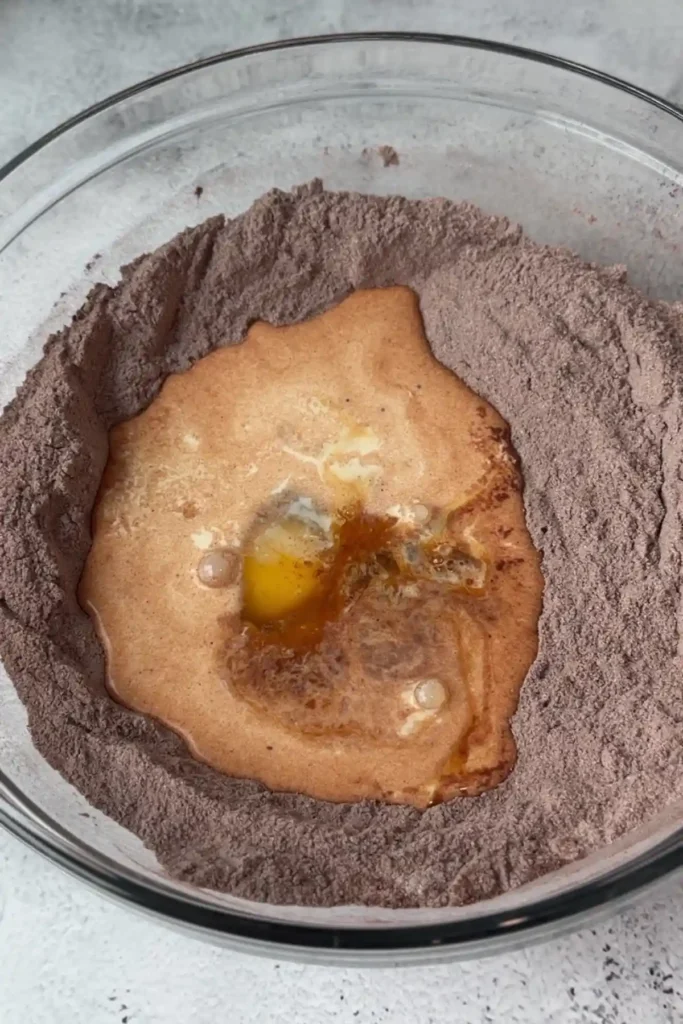 Wet ingredients including egg, oil, and milk mixture added into a well in the center of the dry ingredients before mixing.