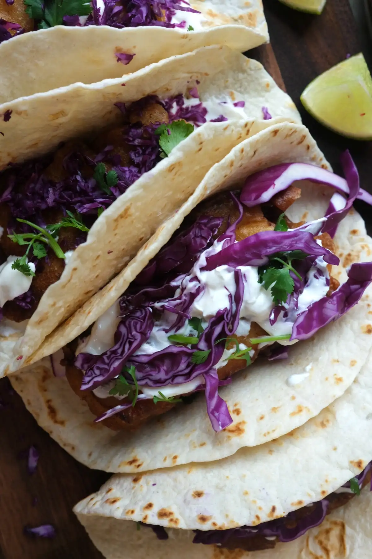 Close-up of cod fish tacos with crispy battered fish, purple cabbage, cilantro, and drizzled sauce in warm tortillas.