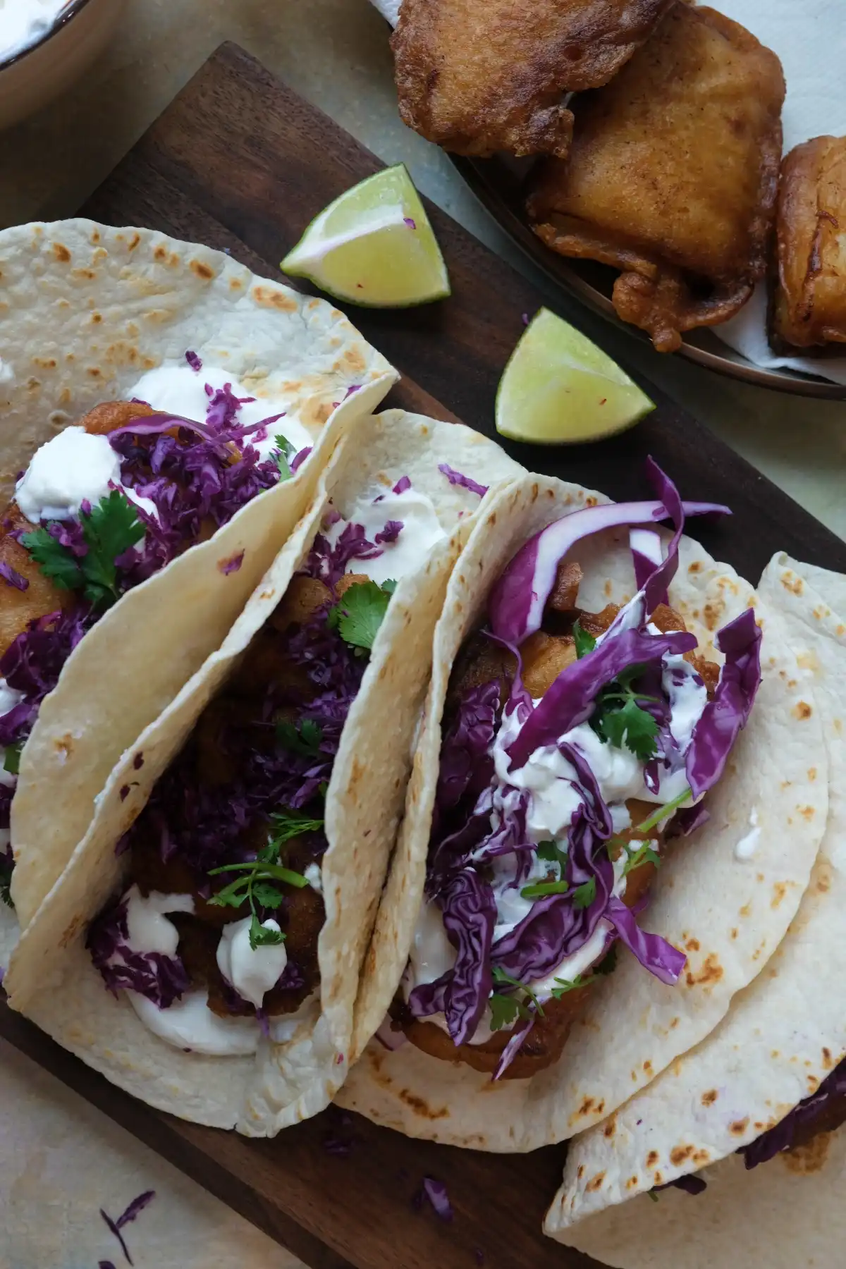 Overhead view of fish tacos with golden fried cod, creamy sauce, cabbage, and lime wedges on the side.