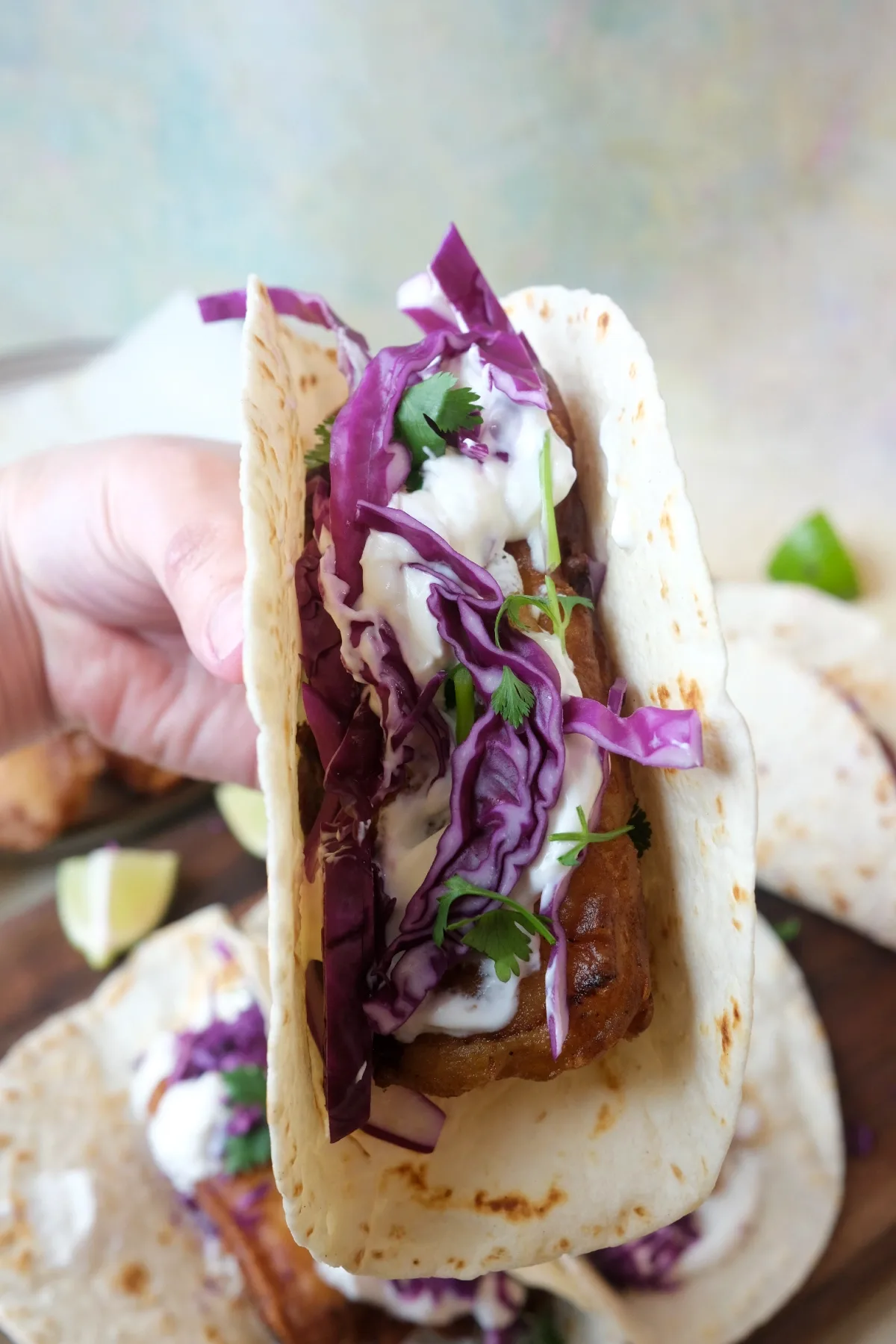 Handheld fish taco filled with crispy cod, cabbage, cilantro, and creamy sauce in a soft tortilla.