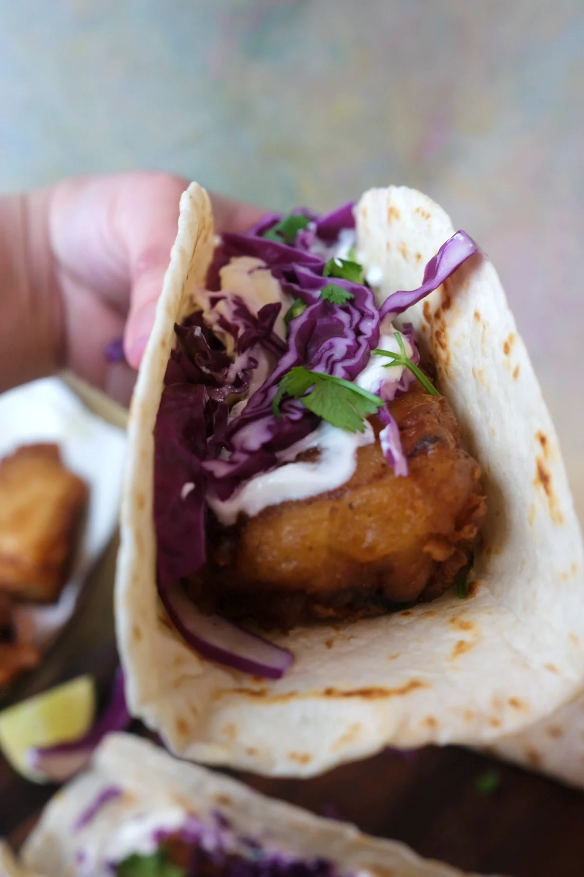 Close-up of a fish taco showing crispy fried cod, shredded cabbage, cilantro, and sauce layered inside a tortilla.