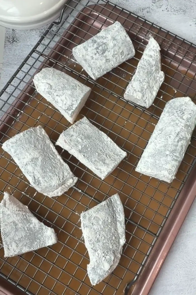 Floured cod fillets arranged on a wire rack before frying
