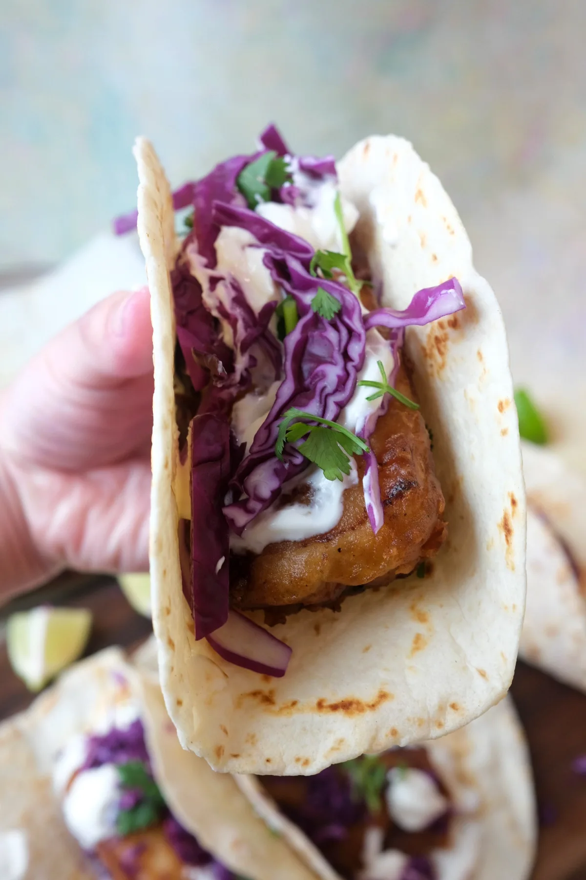Crispy battered cod tacos topped with cabbage, cilantro, and creamy sauce in soft tortillas on a serving board.