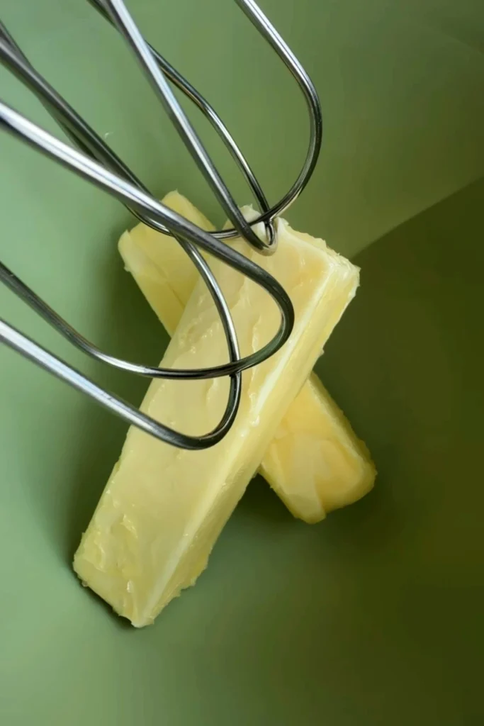Two sticks of softened butter in a mixing bowl with hand mixer beaters, ready to be whipped for the frosting.
