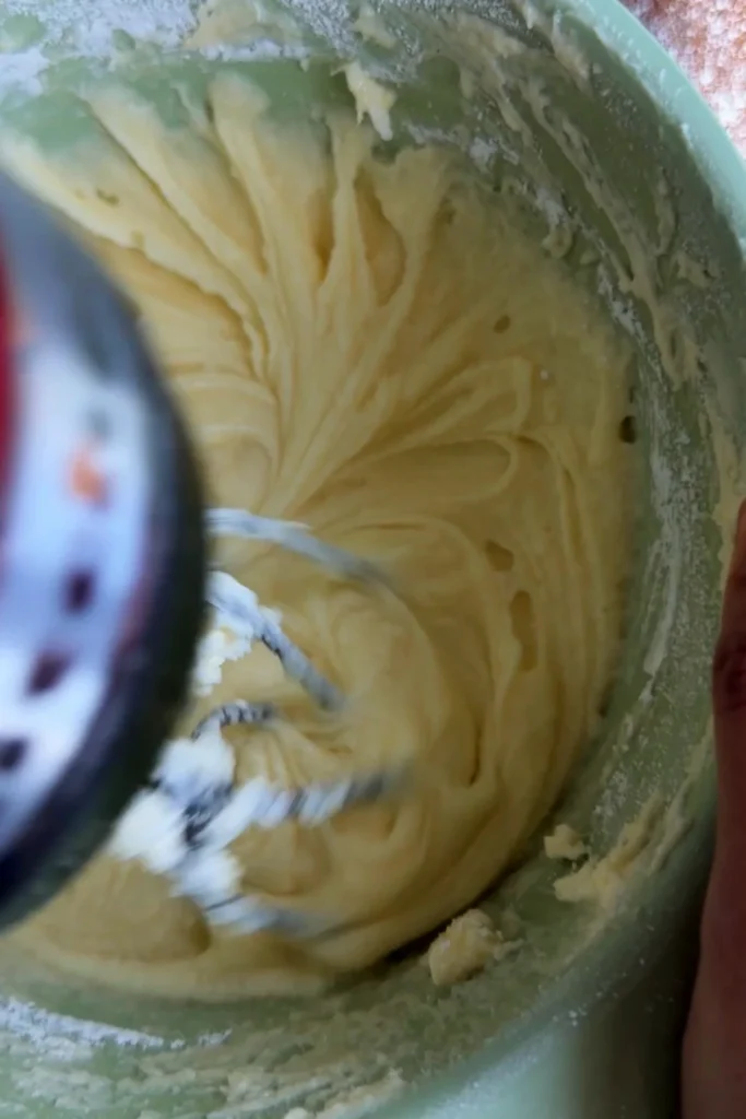 Cream cheese frosting being beaten until smooth and silky, with the mixer creating soft swirls in the bowl.
