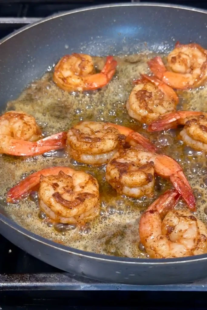 Shrimp seared in a skillet until pink and lightly browned, sitting in hot bubbling butter and oil with caramelized bits forming in the pan.