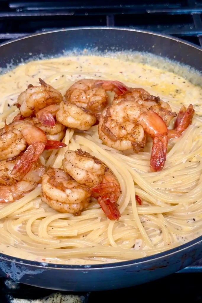Cooked spaghetti and seared shrimp added back into the skillet with the creamy garlic sauce, ready to be tossed until the noodles are fully coated.