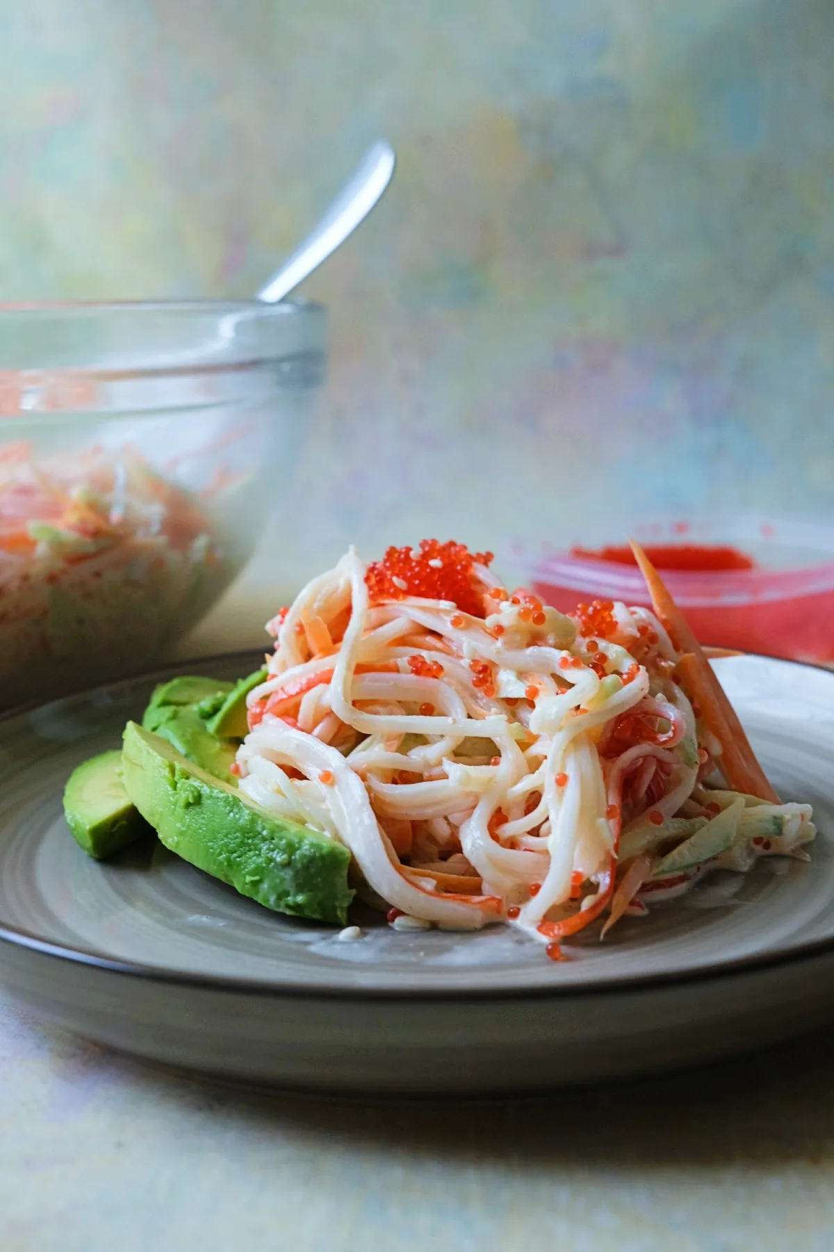 Side view of plated kani salad on a gray plate with avocado slices on the left, topped with orange tobiko.