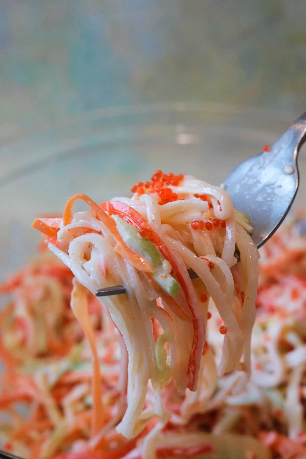 Close-up of a fork holding a bite of spicy kani salad with shredded imitation crab, cucumber, carrot, and tobiko in creamy dressing.