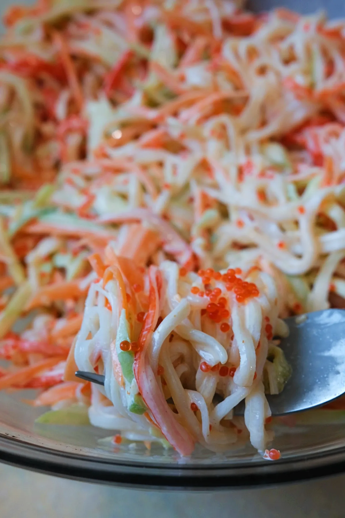 Tight close-up of a forkful of kani salad with imitation crab, julienned vegetables, and orange tobiko.