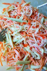 Close-up of the mixed kani salad in a glass bowl, showing shredded imitation crab, julienned cucumber, carrot, and orange tobiko lightly coated in creamy dressing.
