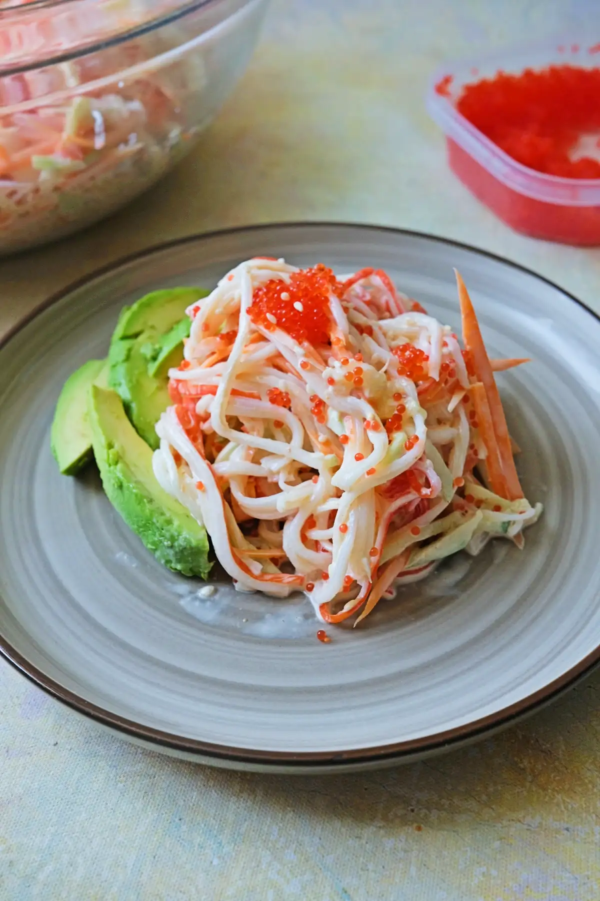 Overhead shot of plated kani salad on a plate with avocado slices on the left, topped with tobiko and a few sesame seeds.