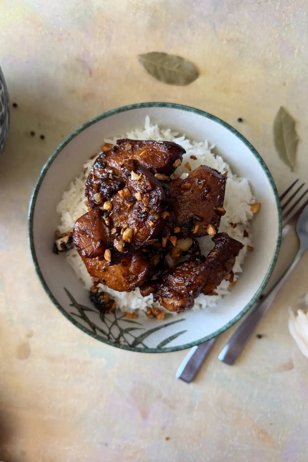 Filipino pork adobo served over white rice in a shallow ceramic bowl with a green rim. 