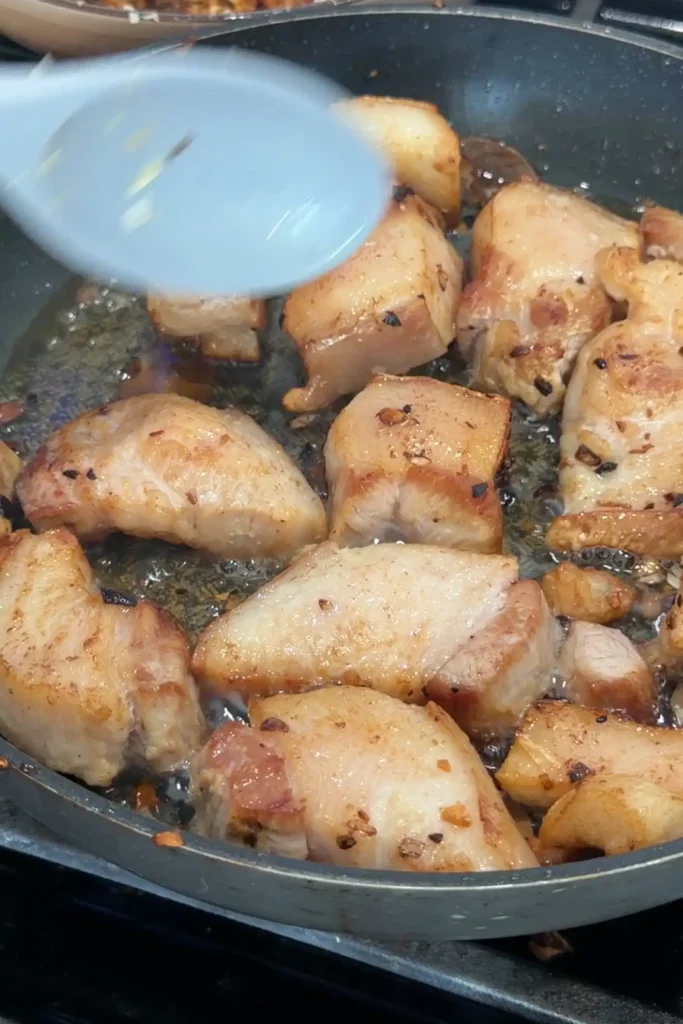 Raw chunks of pork belly browning in the same skillet after the garlic has been taken out.