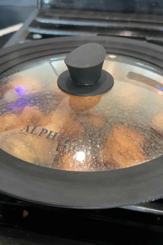 Glass lid covering a skillet of pork adobo as it cooks on the stovetop.