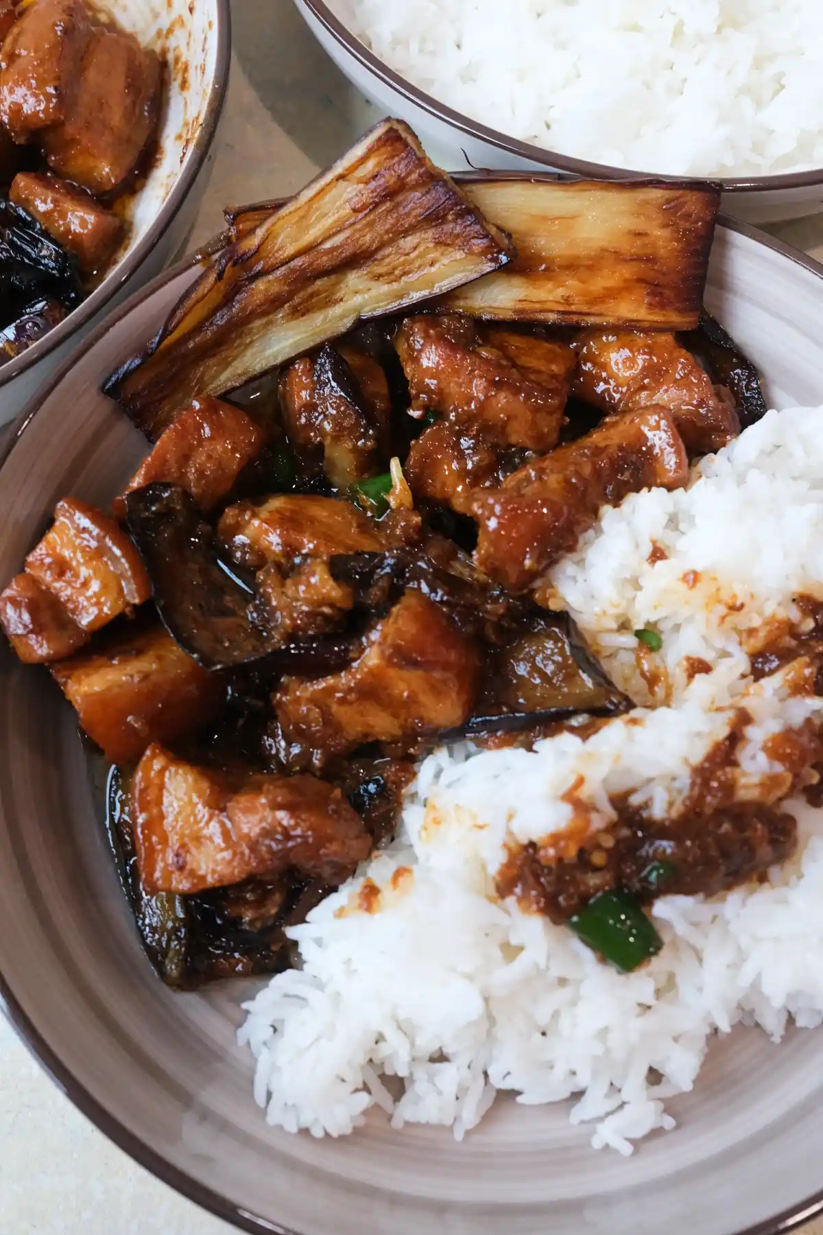 Close overhead shot of pork binagoongan served with white rice, with browned eggplant strips on top and extra sauce spooned over the rice.