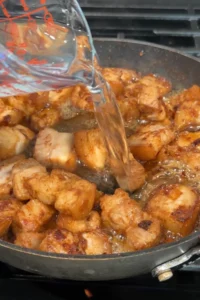 Water being poured from a measuring cup into the skillet with browned pork belly and shrimp paste.