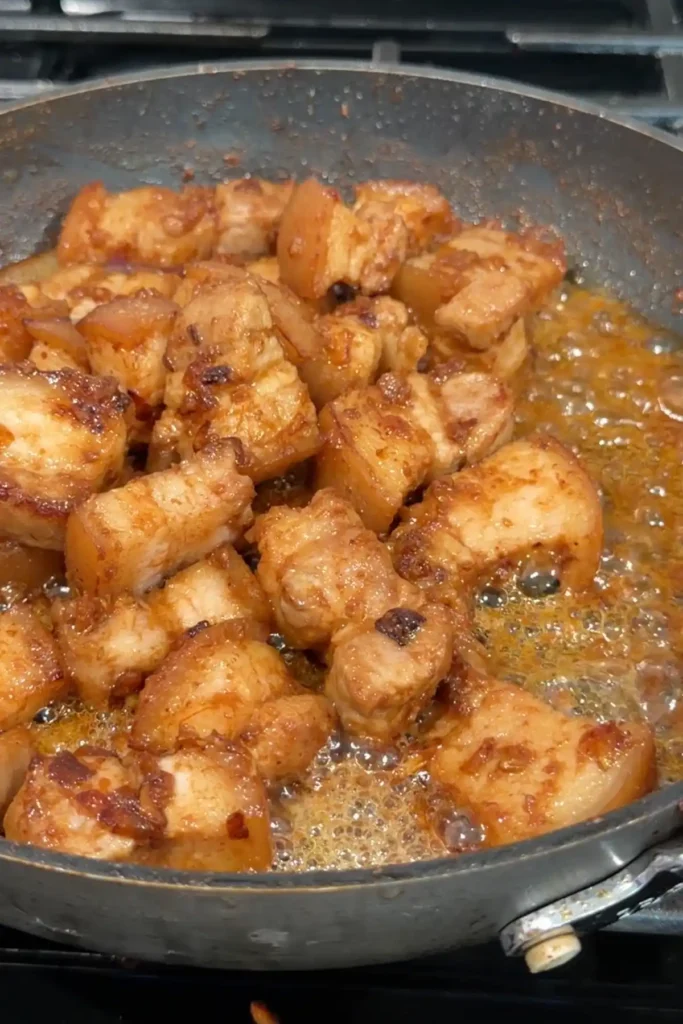 Pork belly simmering in the pan after adding vinegar, with sauce bubbling around the edges.