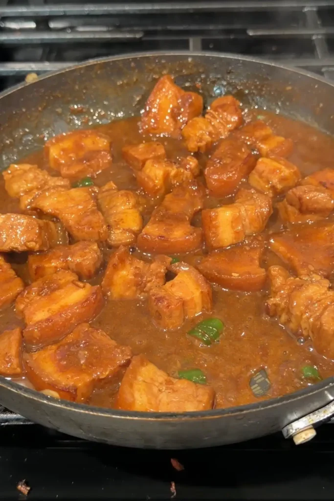 Pork binagoongan simmering in a thicker reddish-brown sauce with green chilies mixed in.