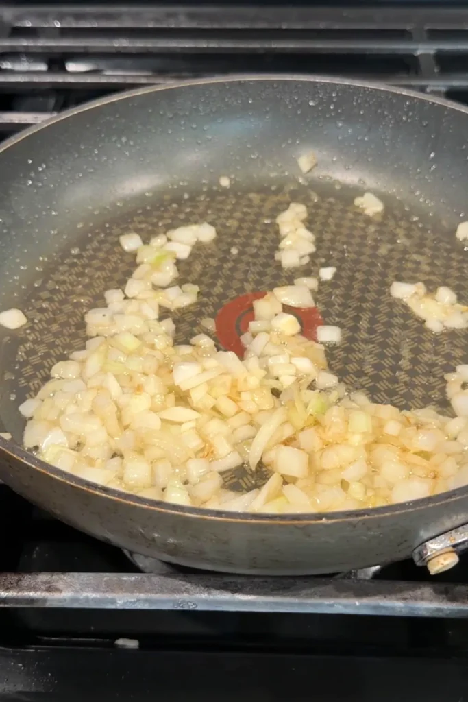 Diced onion sautéing in oil in a skillet, starting to soften and turn translucent.