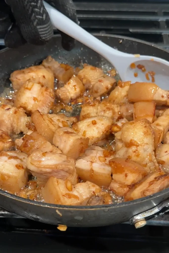 Pork belly stirred in the pan after adding fish sauce, with garlic and onion clinging to the meat.
