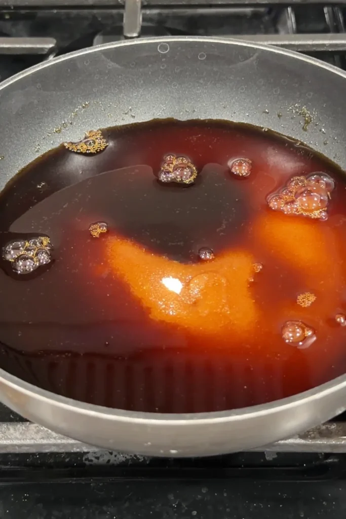 Soy sauce, sugar, and mirin sit in a gray skillet on the stovetop before cooking