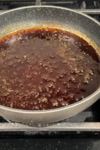 Homemade eel sauce simmers in a gray skillet on the stovetop.