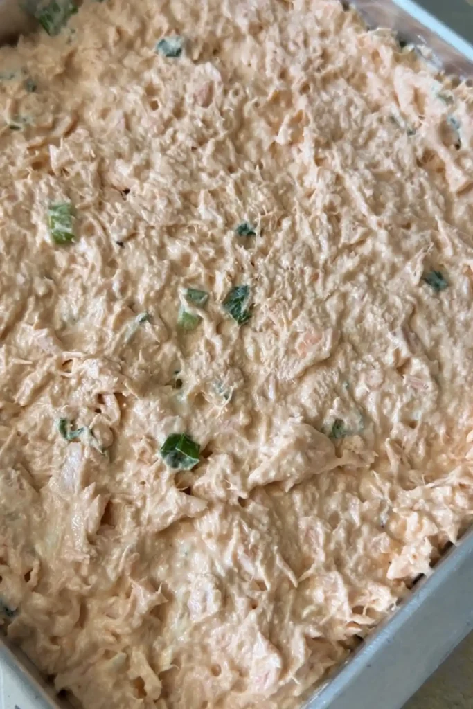 Creamy salmon filling is spread evenly over the rice layer in a rectangular metal pan, with bits of green onion visible throughout.