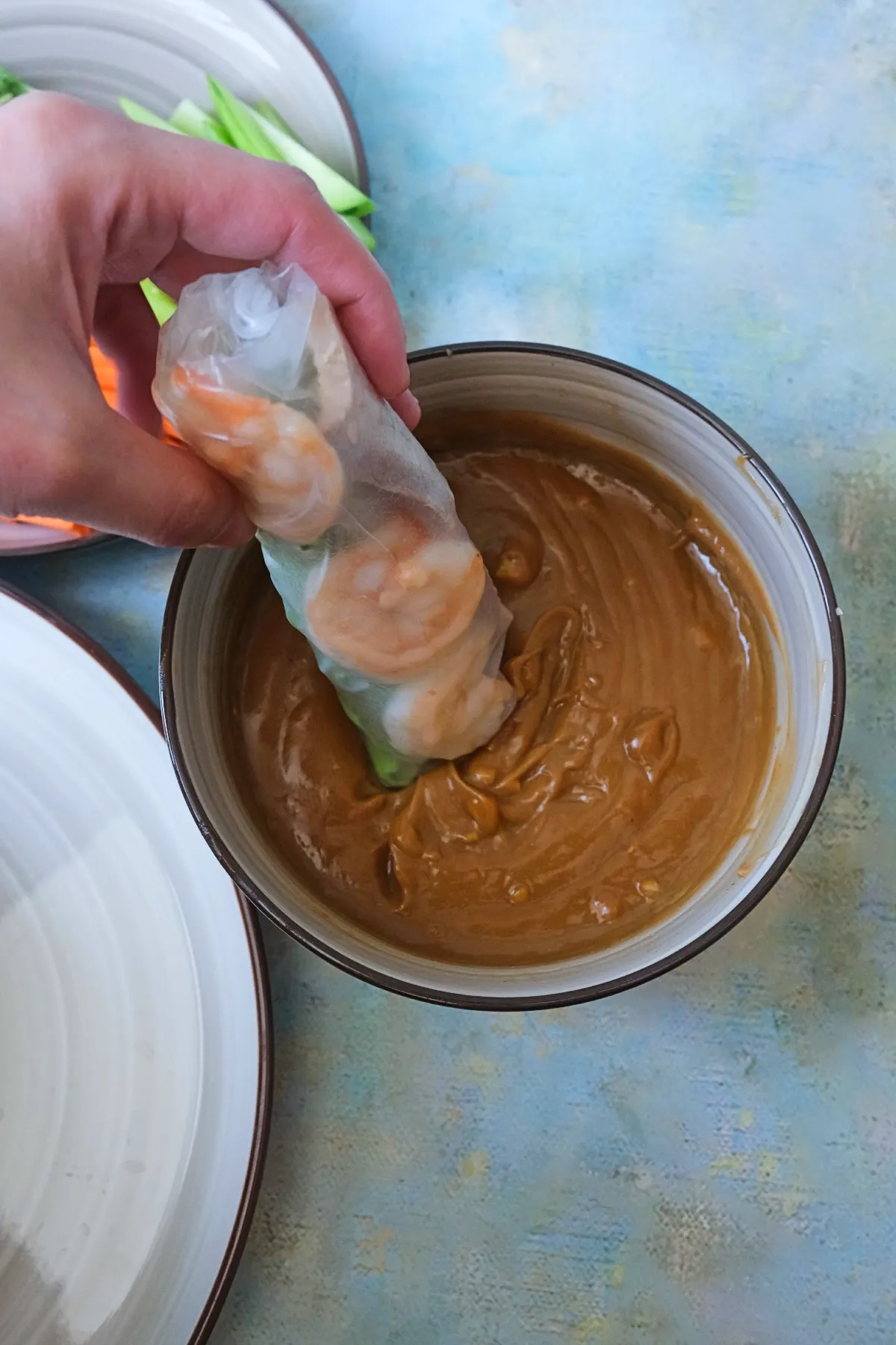 Hand dipping a Vietnamese spring roll into thick peanut sauce