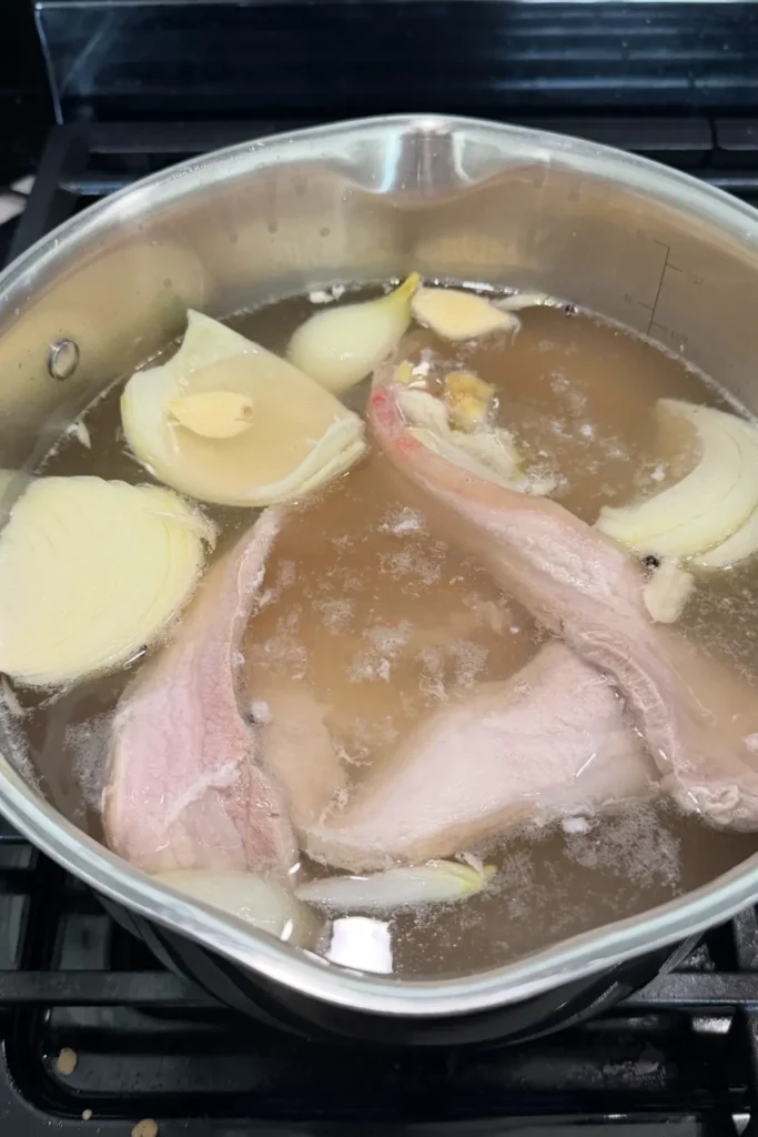 Pork belly simmering in a pot with onion, garlic, and aromatics to make flavorful broth