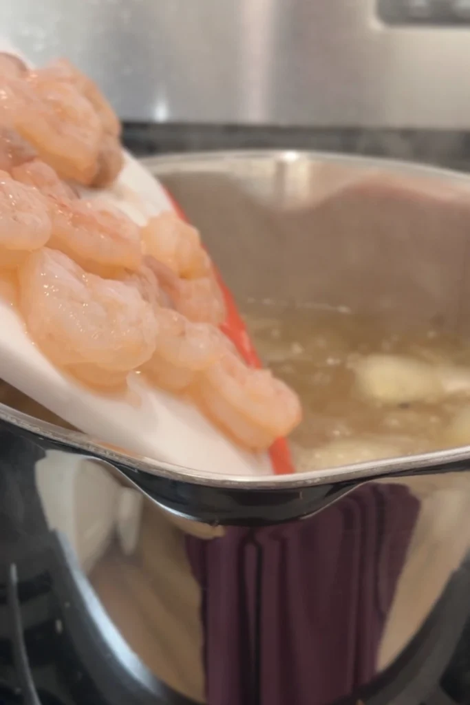 Raw shrimp being added into a pot of hot broth for poaching