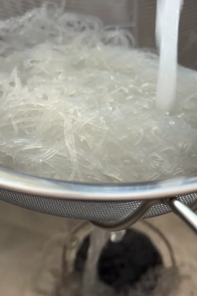 Cooked vermicelli noodles draining in a strainer under running water