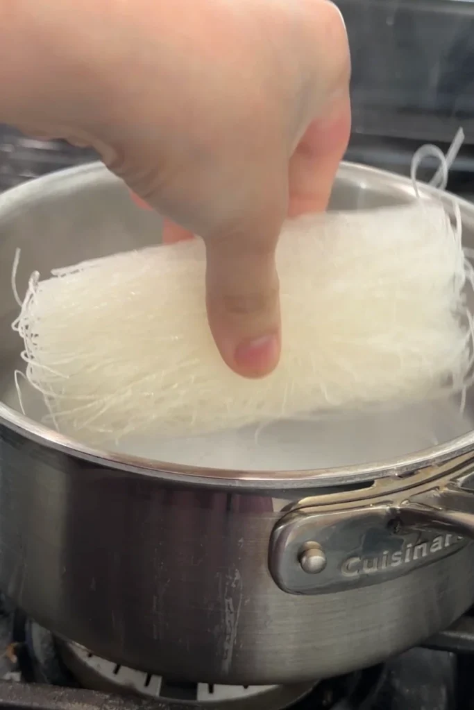 Dry rice vermicelli noodles being lowered into boiling water