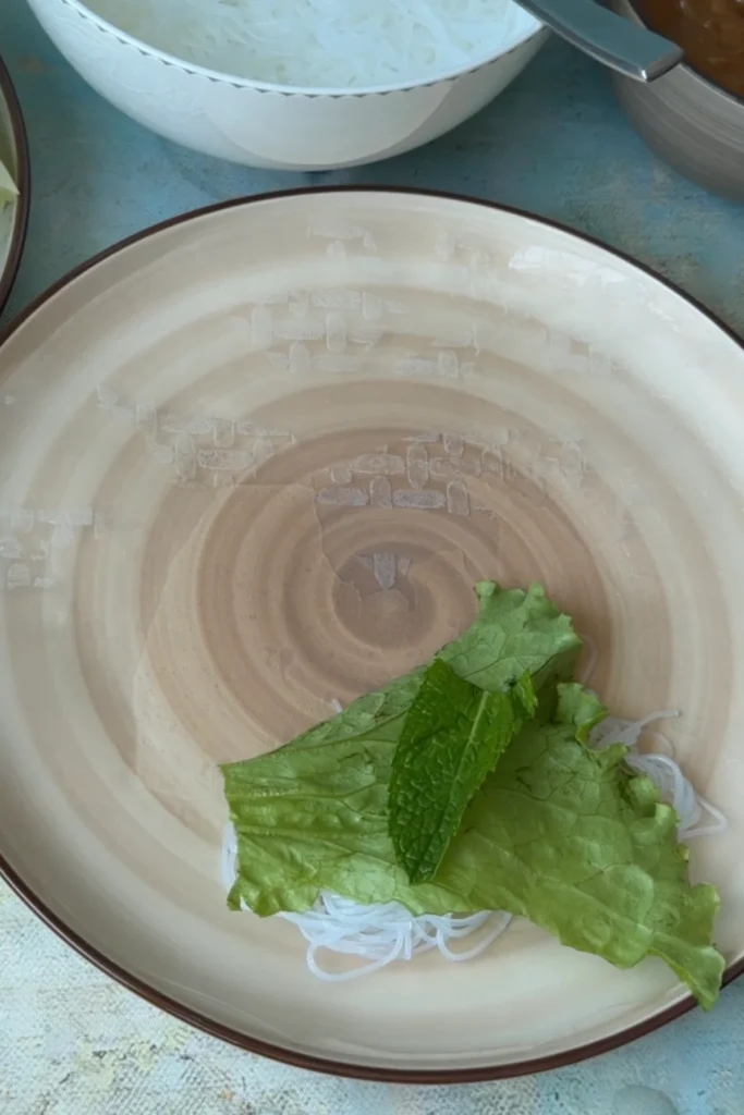 Lettuce and fresh mint layered on top of rice noodles as filling base