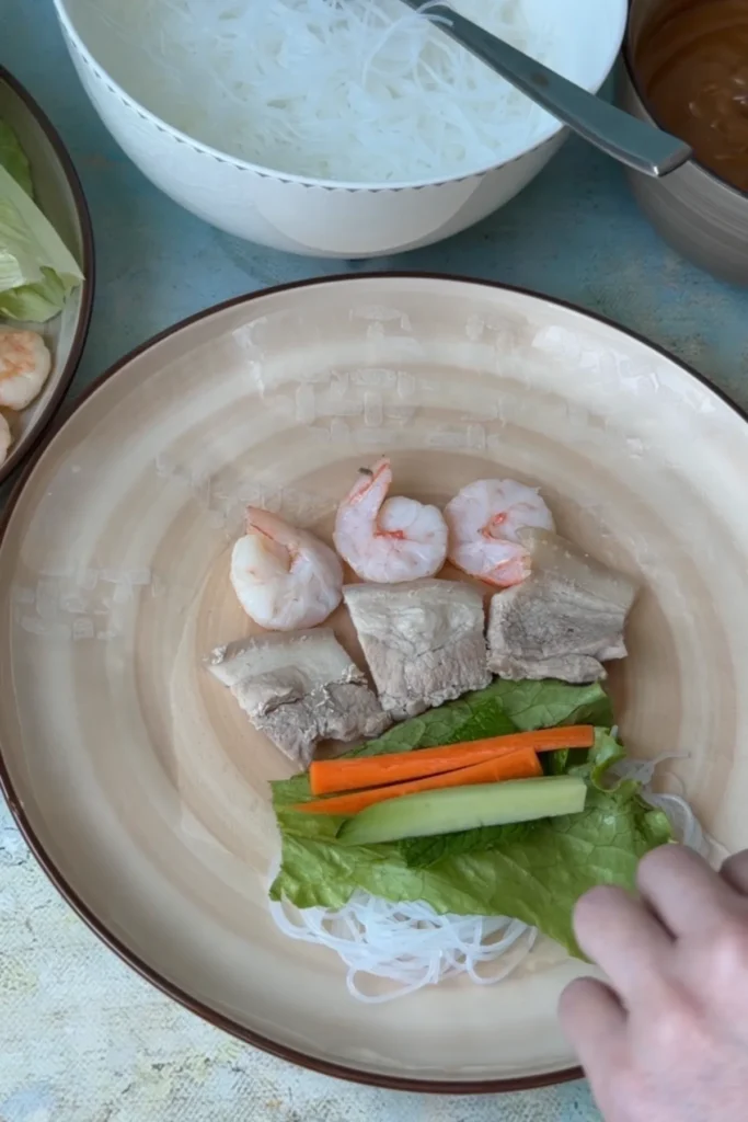 Shrimp, sliced pork, carrots, and cucumber added over herbs and noodles