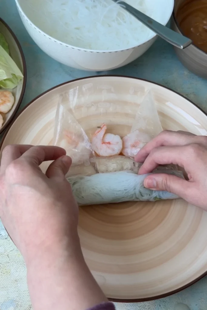 Rolling the spring roll tightly by folding the bottom over the filling