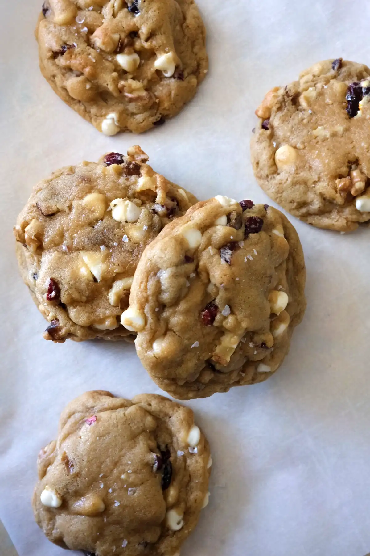 Soft cranberry white chocolate cookies with walnuts scattered on parchment paper, showing thick texture and gooey white chocolate chips.