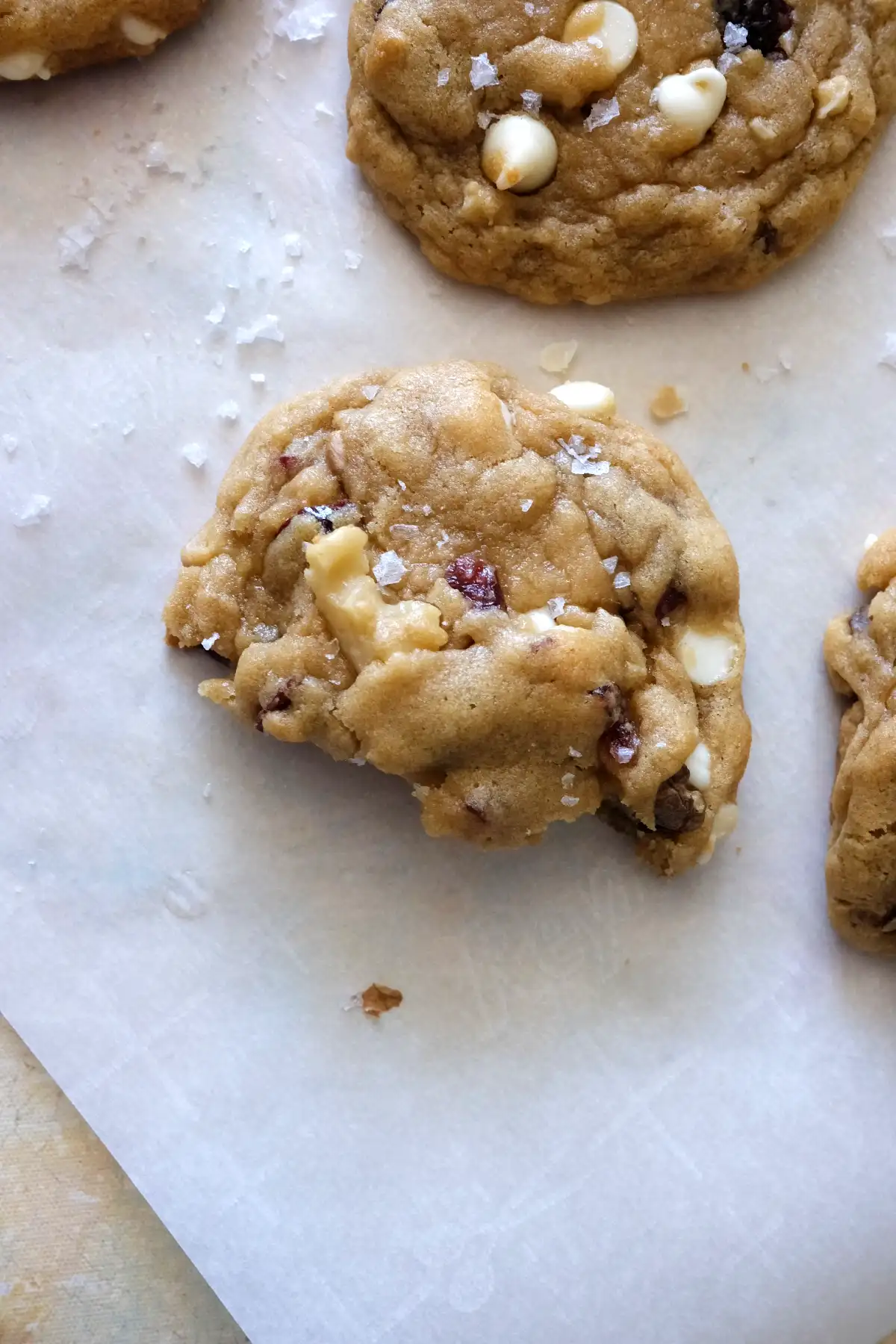 Half-eaten cranberry white chocolate cookie revealing soft interior with melted white chocolate, cranberries, and walnuts.