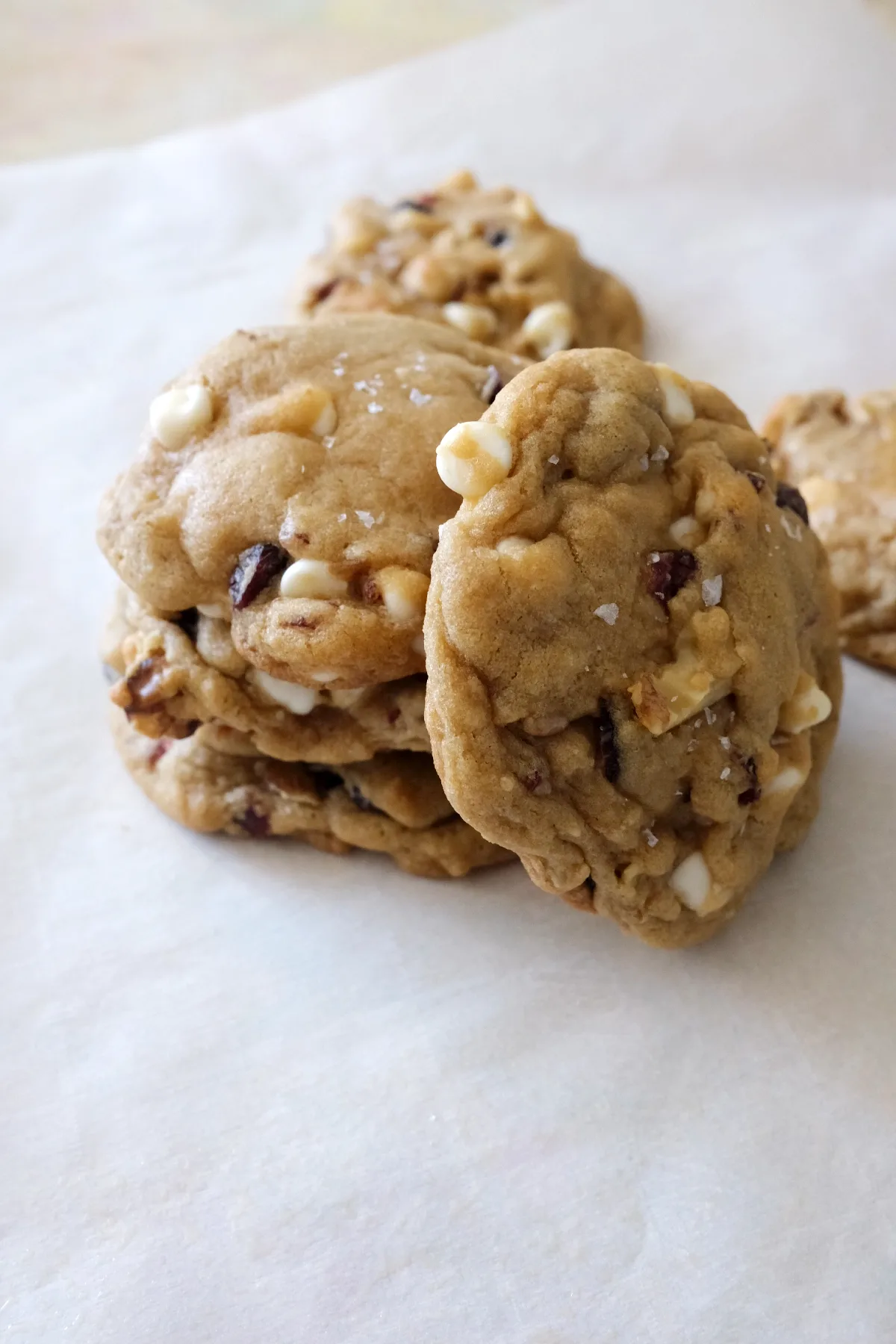 Close-up of cranberry white chocolate cookies on parchment with white chocolate chips, cranberries, and walnuts in every bite.